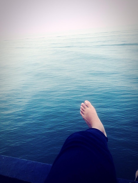 Foto sezione bassa di una persona seduta su una ringhiera sopra il mare contro il cielo