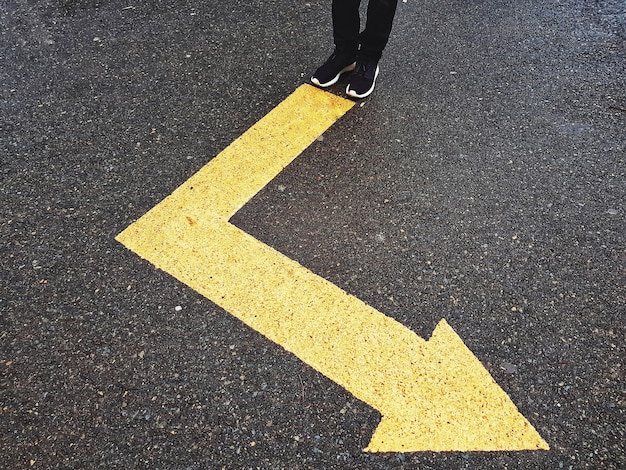 Photo low section of person standing on arrow symbol at road