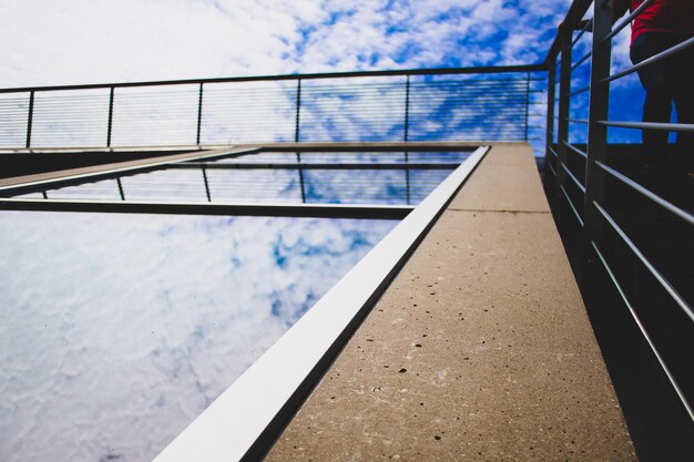 Photo low section of person walking by railing of modern building against cloudy sky