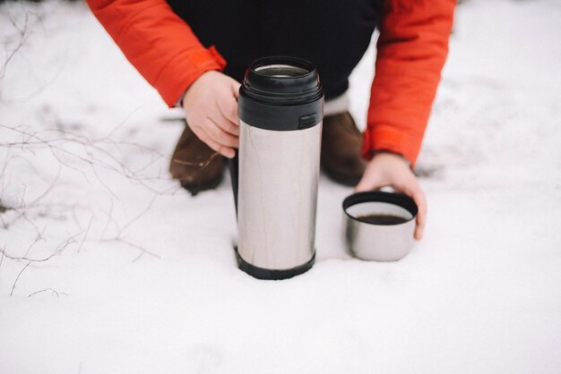 Low section of person with tea on snow covered field