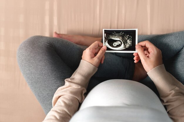 Low section of pregnant woman holding ultrasound image