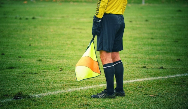 Photo low section of referee holding flag while standing on sports field