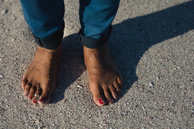 Low section of a senior African American woman standing on the beach with bare feet and red painted toenails during a sunny day