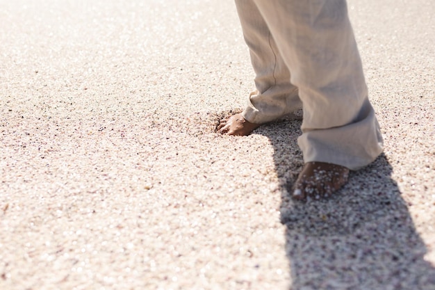 Low section of senior biracial woman standing barefoot on sand at beach during sunny day. lifestyle and weekend