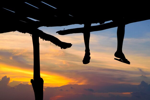 Foto sezione bassa della silhouette di una persona seduta sul molo contro un cielo nuvoloso