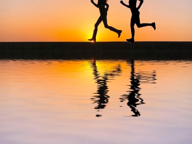 Low section of silhouette women running by lake against sky during sunset