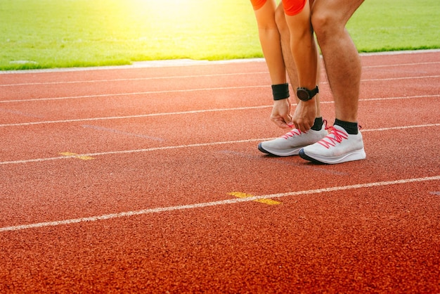 Foto sezione bassa di uno sportivo che lega i lacci delle scarpe sulla pista da corsa