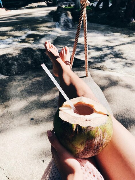 Photo low section of woman holding coconut while lying on hammock