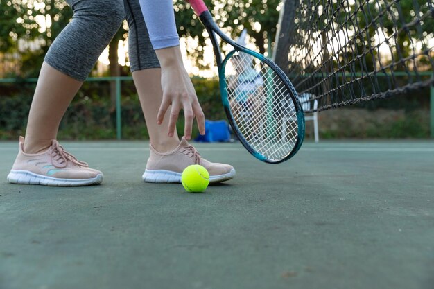 屋外テニスコートでボールを拾うテニスラケットを持つ女性の低いセクション、コピースペース付き