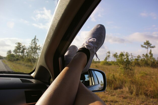 Photo low section of woman legs on car window by field against sky