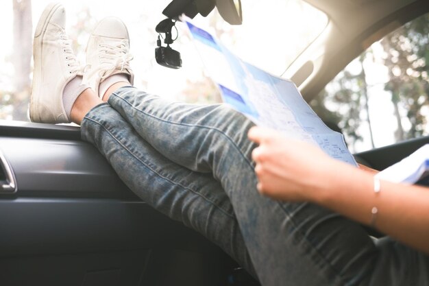 Foto sezione bassa delle gambe della donna sul cruscotto mentre tiene la mappa in macchina