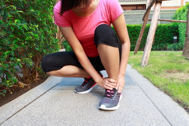 Photo low section of woman massaging foot while sitting on footpath at park