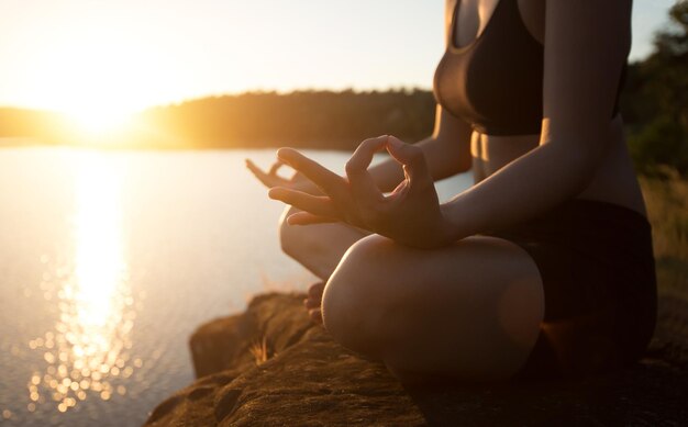 Photo low section of woman meditating while sitting on rock at lakeshore during sunset