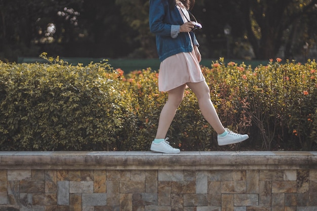 Photo low section of woman photographing leg while standing on retaining wall by plants