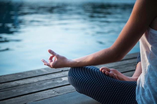 low section of woman practicing yoga on pier over lake