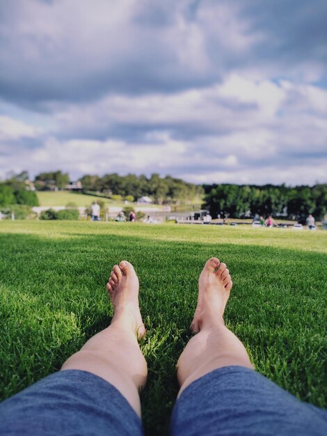 Low section of woman relaxing on grass against sky