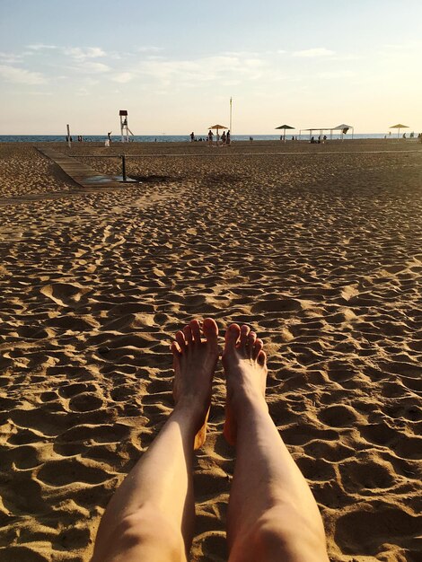 Low section of woman relaxing on sand at beach against sky