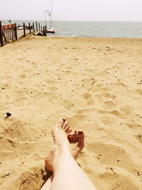 Low section of woman sitting at beach against sky