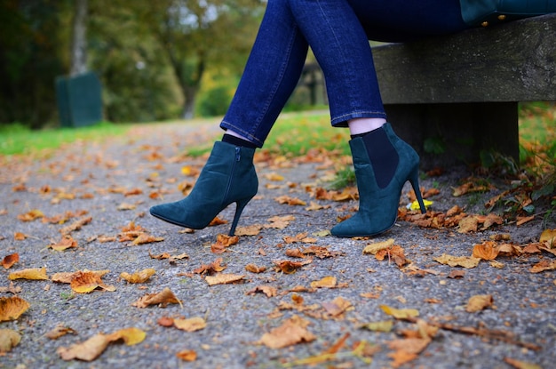 low section of woman sitting on bench by autumn leaves on street