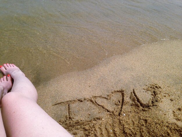 Photo low section of woman sitting by text on sand at beach