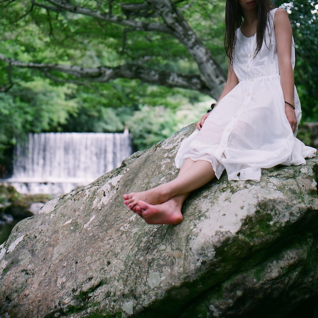 Low section of woman sitting on rock at forest