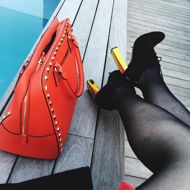 Photo low section of woman sitting with orange purse on boardwalk