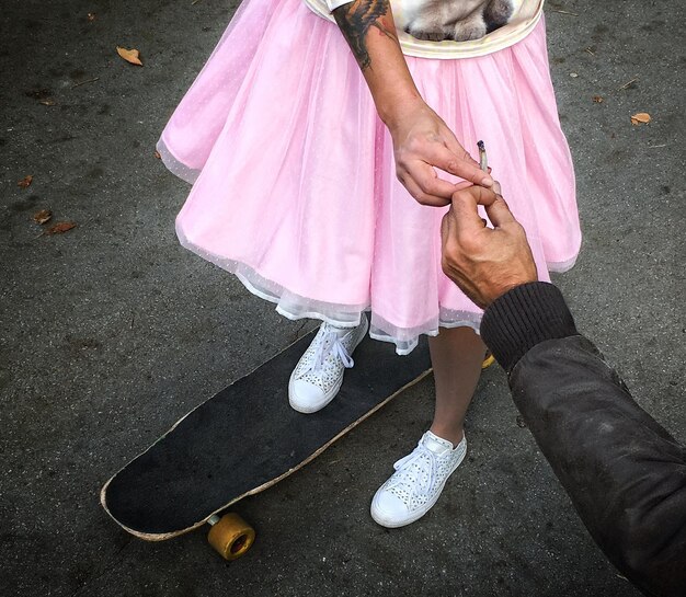 Foto sezione bassa di una donna su uno skateboard che prende una canna da un uomo