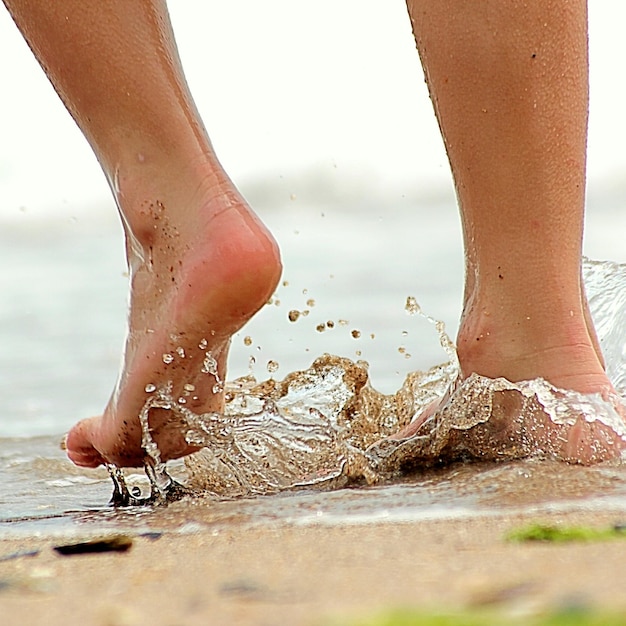 Low section of woman splashing water on shore at beach