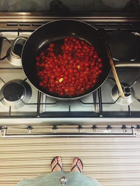 Foto sezione bassa della donna in piedi vicino alla stufa mentre i pomodori a ciliegio cucinano in cucina