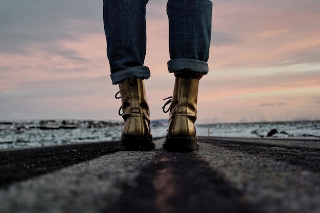 Low section of woman standing on road against sky during sunset