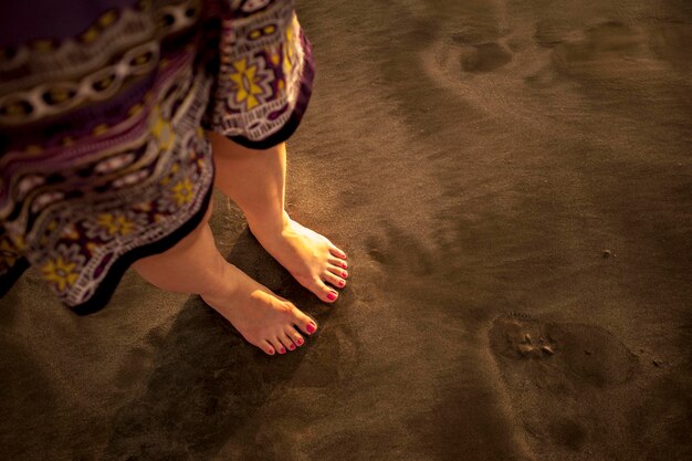 Foto sezione bassa di una donna in piedi sulla spiaggia di sabbia