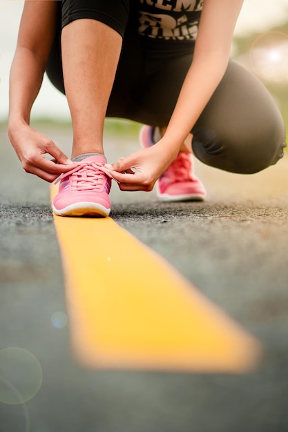 Foto sezione bassa di una donna che lega i lacci delle scarpe mentre si accovaccia sulla strada