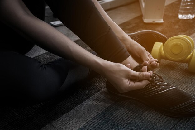 Foto sezione bassa di una donna che lega i lacci delle scarpe mentre è seduta sul tappeto in palestra