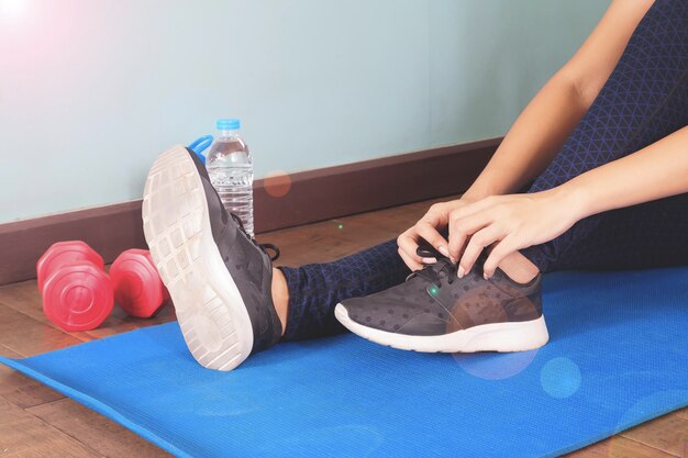 Photo low section of woman tying shoelace while sitting on exercising mat