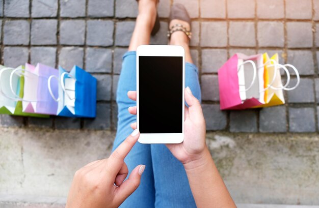 Foto sezione inferiore della donna che usa il telefono cellulare in mezzo alle borse della spesa in città