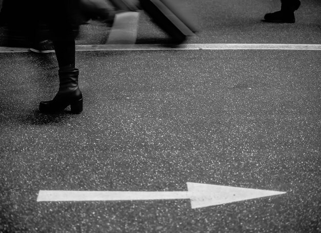 Foto sezione bassa di una donna che cammina con il simbolo della freccia sulla strada