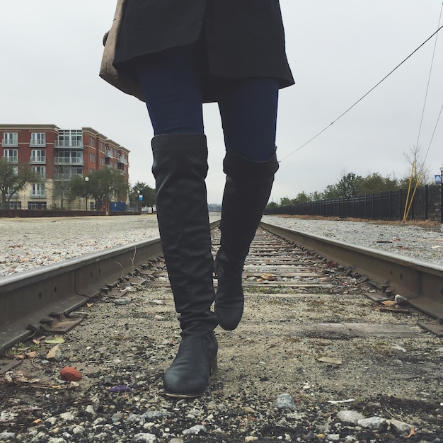 Foto sezione bassa di una donna che cammina sul binario ferroviario contro il cielo