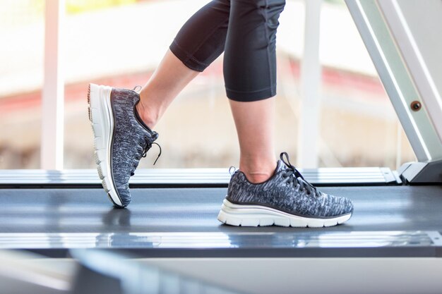 Low section of woman walking on treadmill in gym