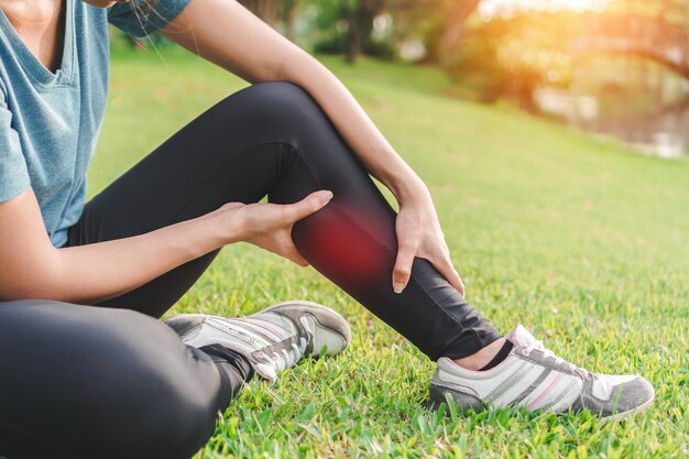 Low section of woman with leg pain sitting on grassy field