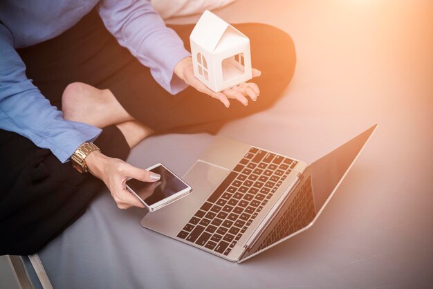 Photo low section of woman with model house and technologies sitting on bed at home