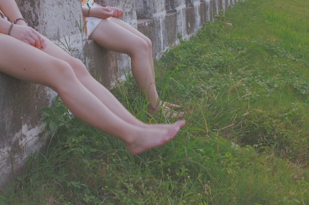 Photo low section of women sitting on retaining wall