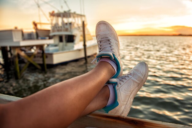 Low section of young woman on railing by sea during sunset