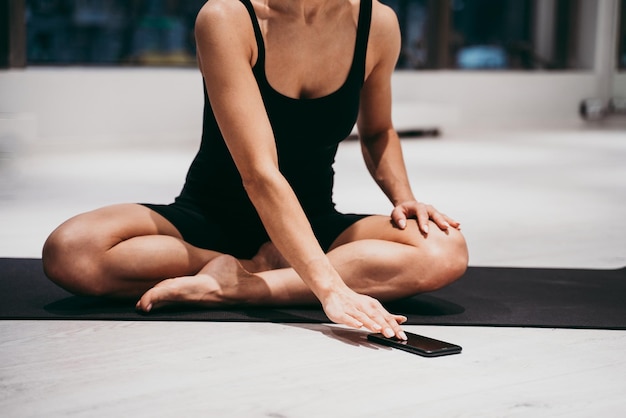 Foto sezione bassa di una giovane donna seduta sul tappetino mentre usa il cellulare in palestra