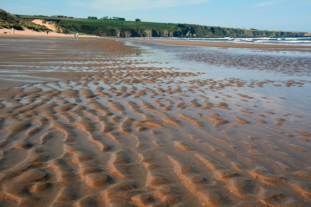 Low tide on a very wide sandy sea beach with holes and pools of water