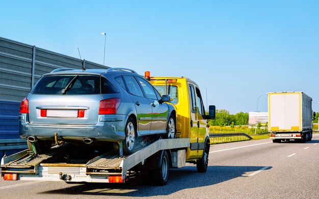 Photo low tow truck trailer with car in road. auto vehicle with carrier transporter hauler on driveway. european transport logistics at haulage work transportation. haul on highway.