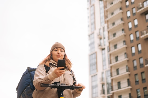 Lowangle view of delivery woman with thermo backpack using navigation app on mobile phone