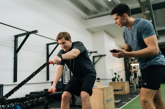 Foto vista a basso angolo di un personal trainer che allena uno sportivo principiante a eseguire le corde di battaglia crossfit