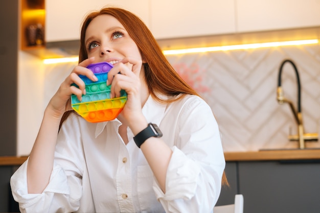 Foto vista dall'angolo basso di una giovane donna sorridente e affascinante dai capelli rossi che spinge silicone morbido iridescente colorato