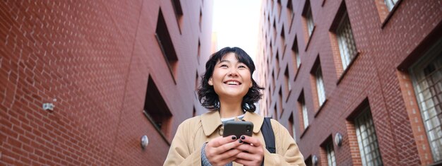 Photo lower angle view of brunette korean girl listening music in headphones walking along street and