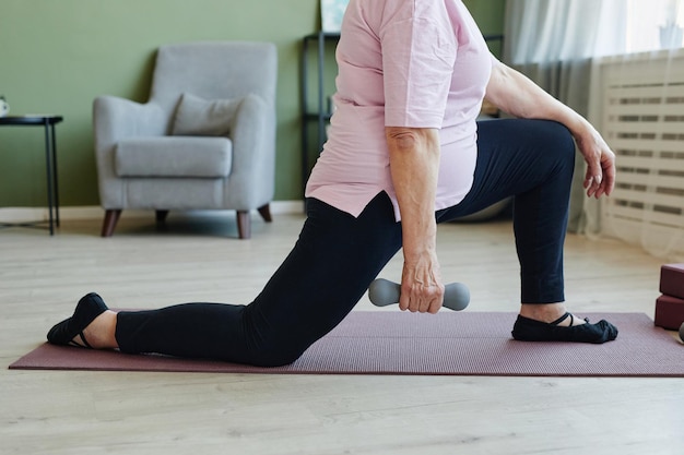 Lower part of active senior woman holding dumbbell during physical exercise